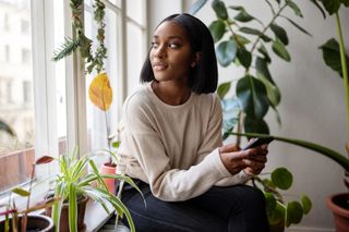 Woman sitting in her living room holding phone and surrounded by plants