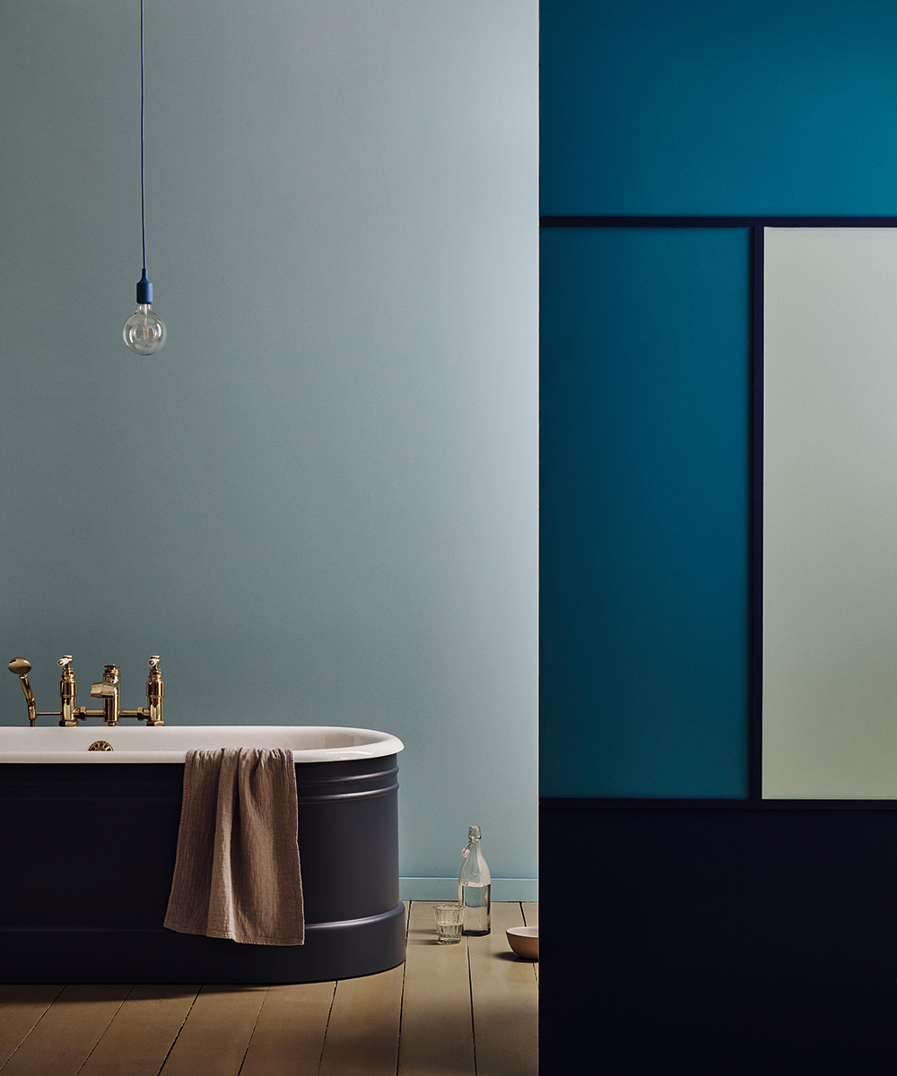 A dark bathroom with walls painted in shades of blue and a bath in the background