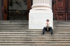 A stressed man is sitting on the steps of the courthouse. The picture represents the frustration of the probate process.