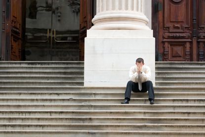 A stressed man is sitting on the steps of the courthouse. The picture represents the frustration of the probate process.