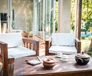 teak furniture set on modern patio in front of home with lots of glazing