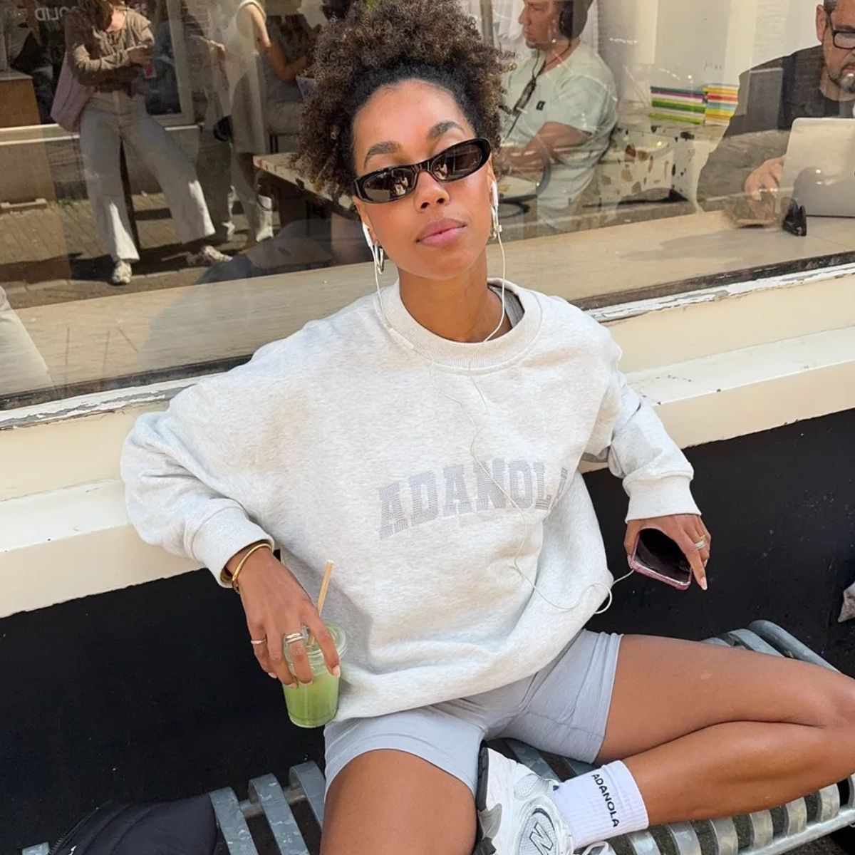 A woman sitting outside a coffee shop in gym gear with a high ponytail hairstyle
