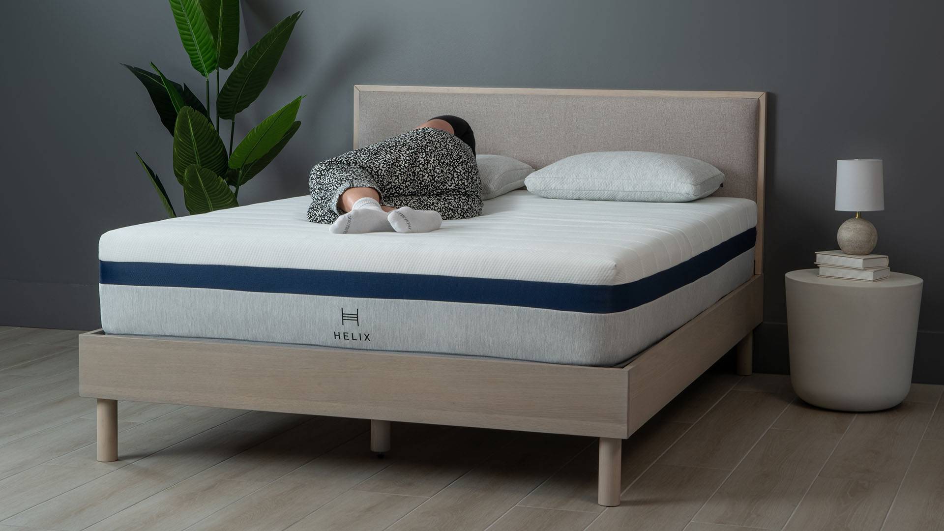 Helix Midnight mattress on a wooden bedframe, against a dark wall
