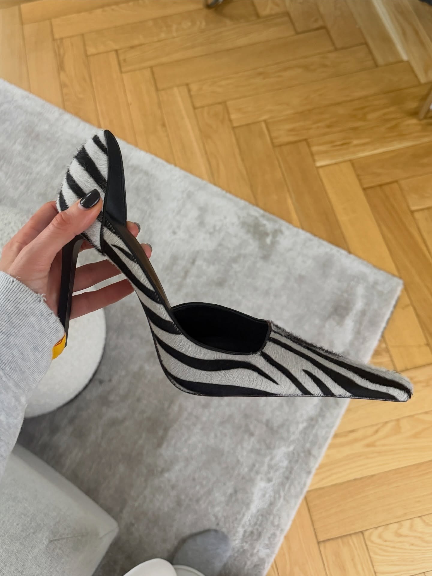 A woman holding a zebra print heel with a short black manicure