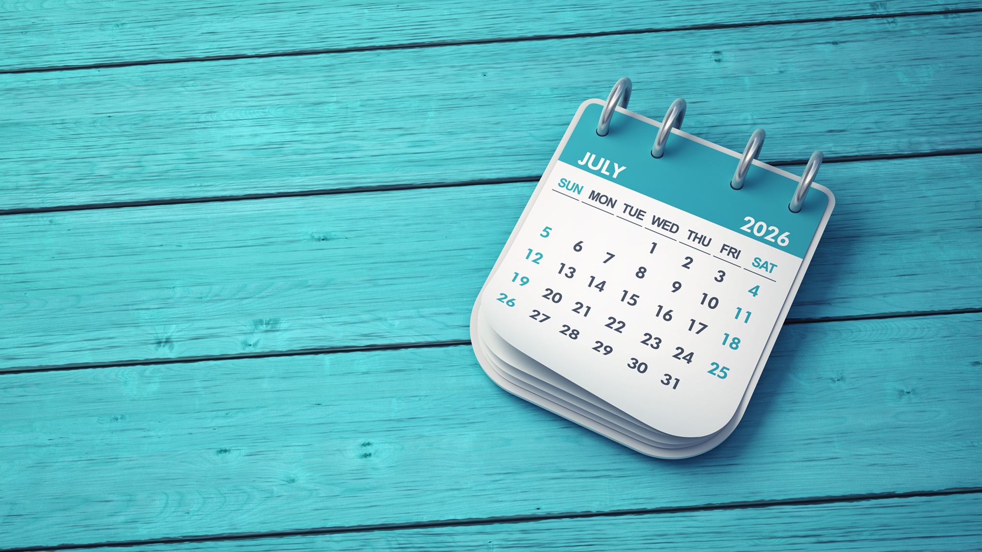 Desk calendar showing July 2026 against turquoise wooden background.