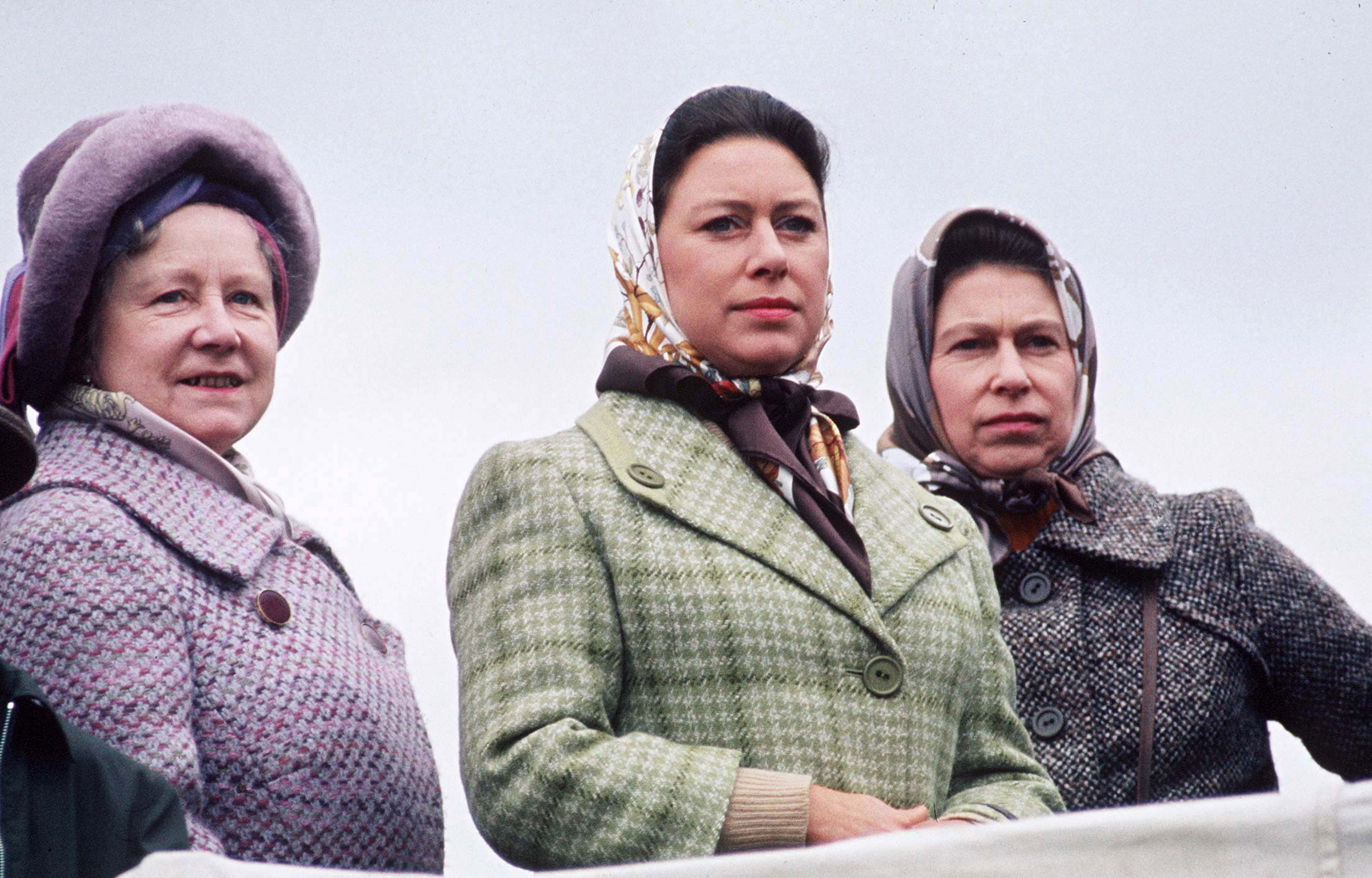 The Queen Mother, Princess Margaret and Queen Elizabeth wearing head scarfs and coats standing in a row