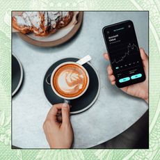 A photo of a hand holding a cup of latte while the other hand checks investments from a smartphone.