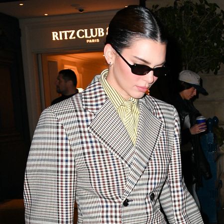 Kendall Jenner in Paris during Paris Fashion Week wearing a Bottega Veneta checkered jacket, jacquard striped shirt and tie, and wool trousers.