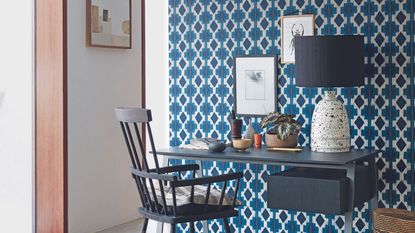 Black office desk and chair against blue patterned wallpaper next to doorway