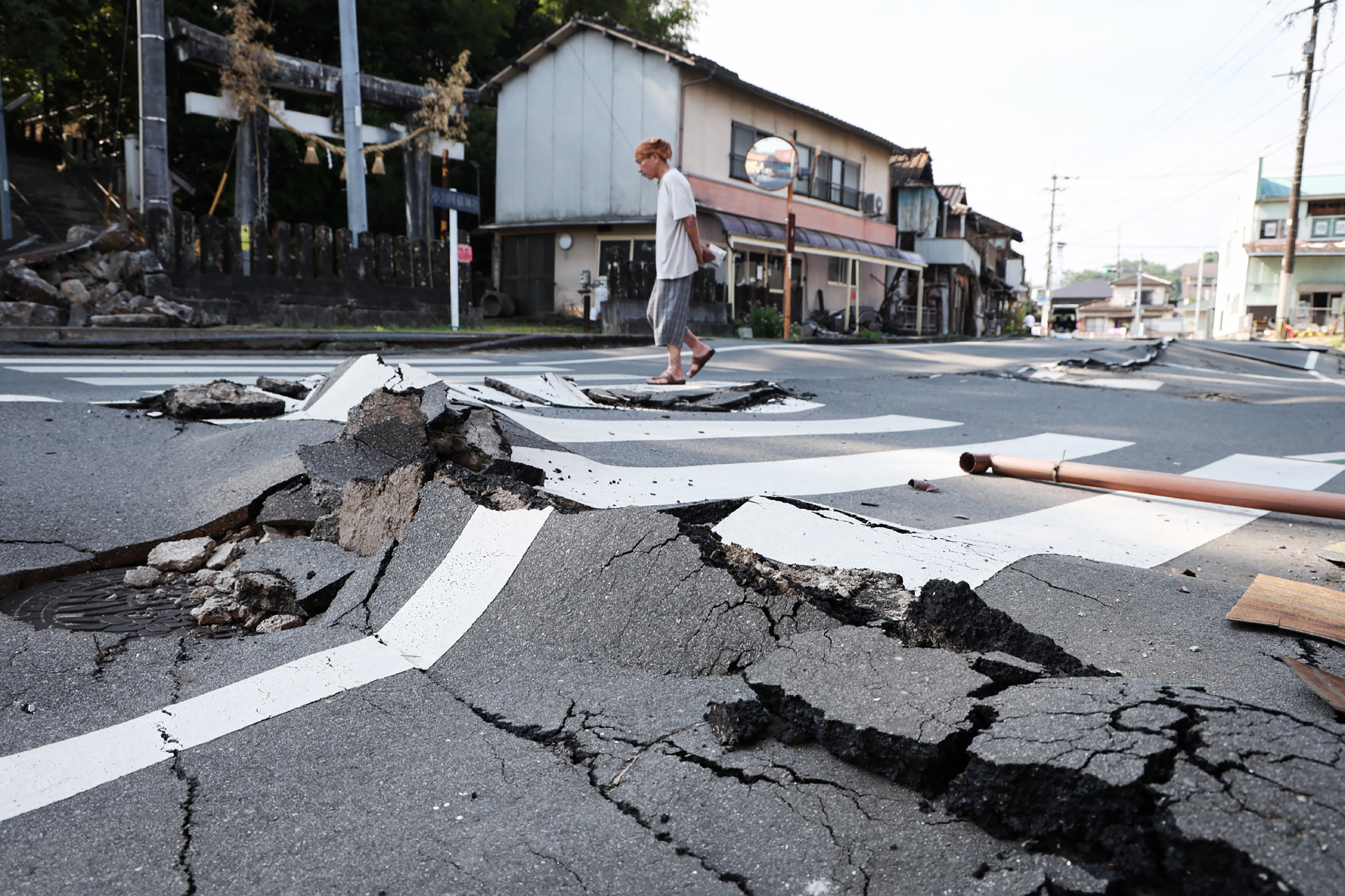 A man walks along a destroyed road in Uki, Kumamoto prefecture on August 3, 2026, following the July 28 earthquake. (Photo by JIJI PRESS / AFP) / Japan OUT