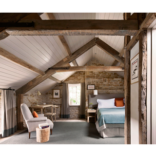 hotel bedroom with stone wall bed white chair and wooden beams on ceiling