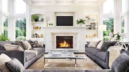A large living room, filled with natural light. Two gray sofas and a white fireplace.