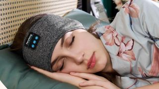 A woman wearing grey Preylong sleep headband sleeping on side in bed with floral pyjamas