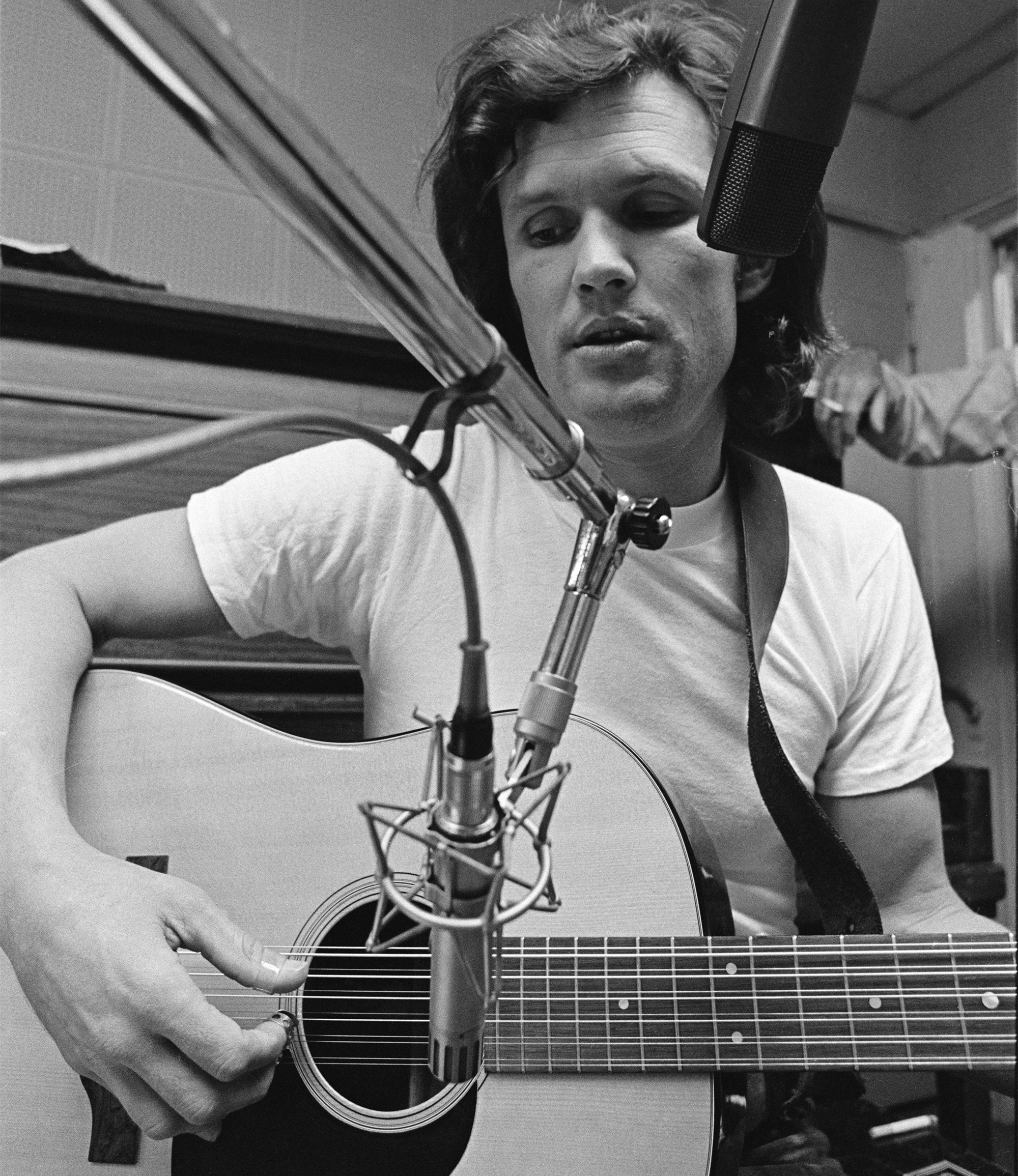 Actor, singer, songwriter, musician, Kris Kristofferson wearing a white T shirtsits on a piano bench with a microphones in front of him while playing an acoustic twelve string guitar at Combine Studios in Nashville, Tennessee in 1970..
