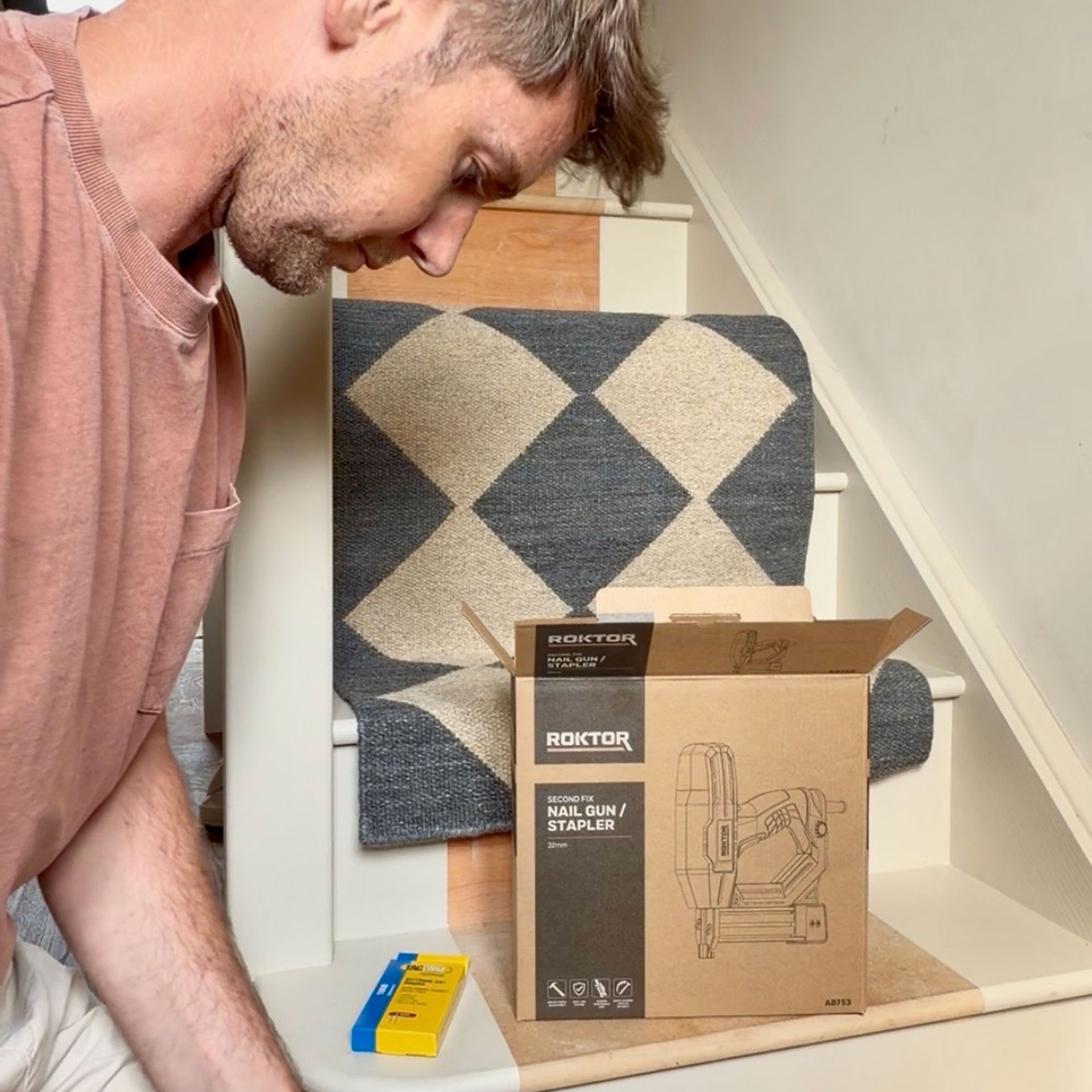 Man kneeling by staircase with runner resting on it by nail gun box