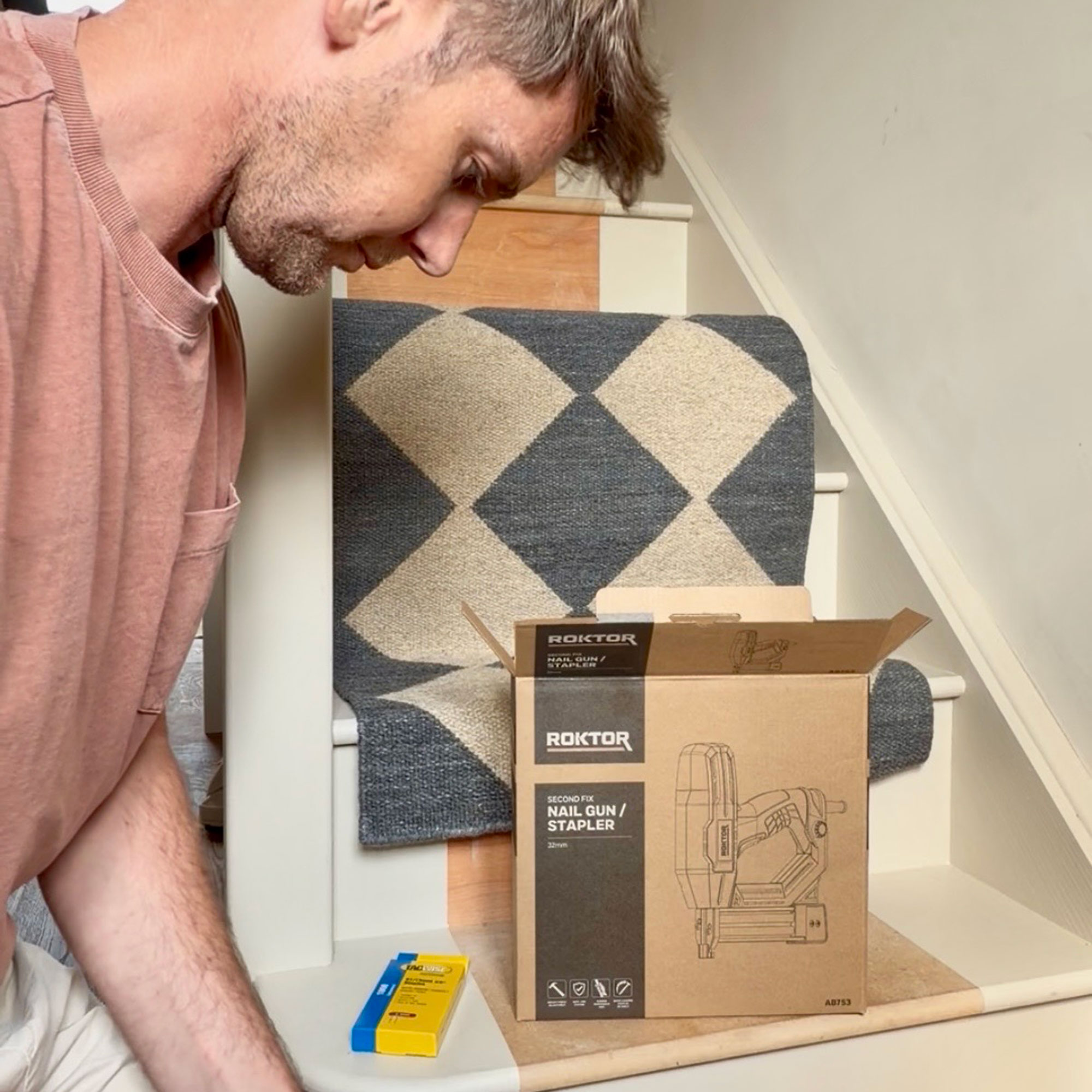 Man kneeling by staircase with runner resting on it by nail gun box