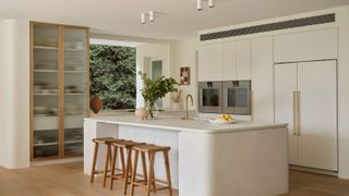 a modern white kitchen with an island, two ovens, and a reeded glass and brass cabinet