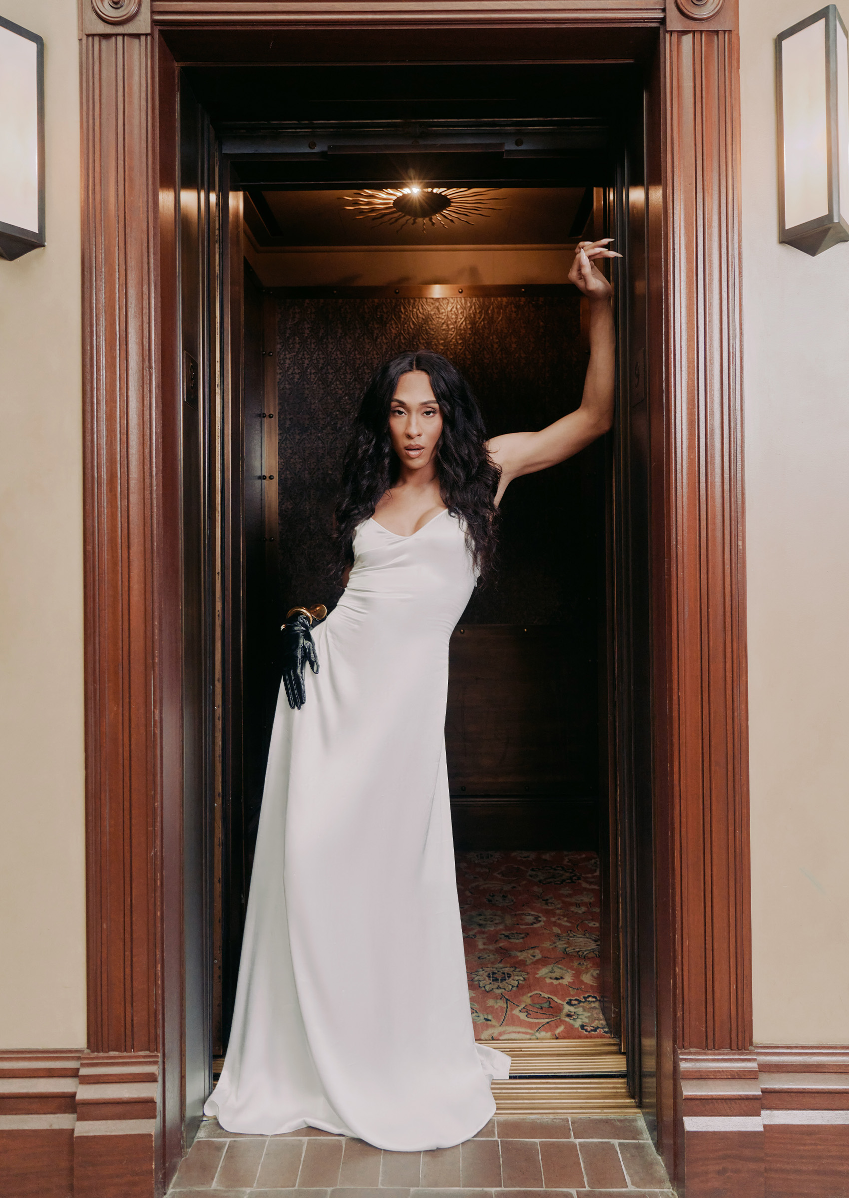 michaela j rodriguez wears a white satin gown and poses in an elevator