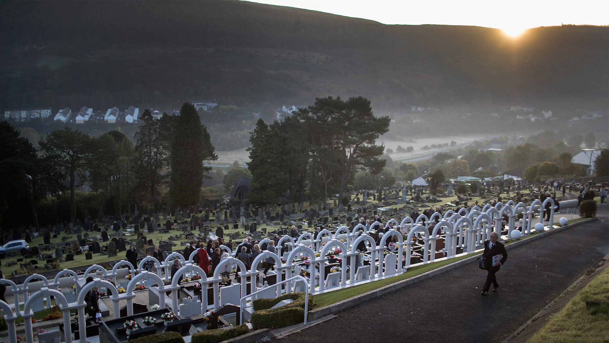 Sun sets as a man walks along a cemetery path.