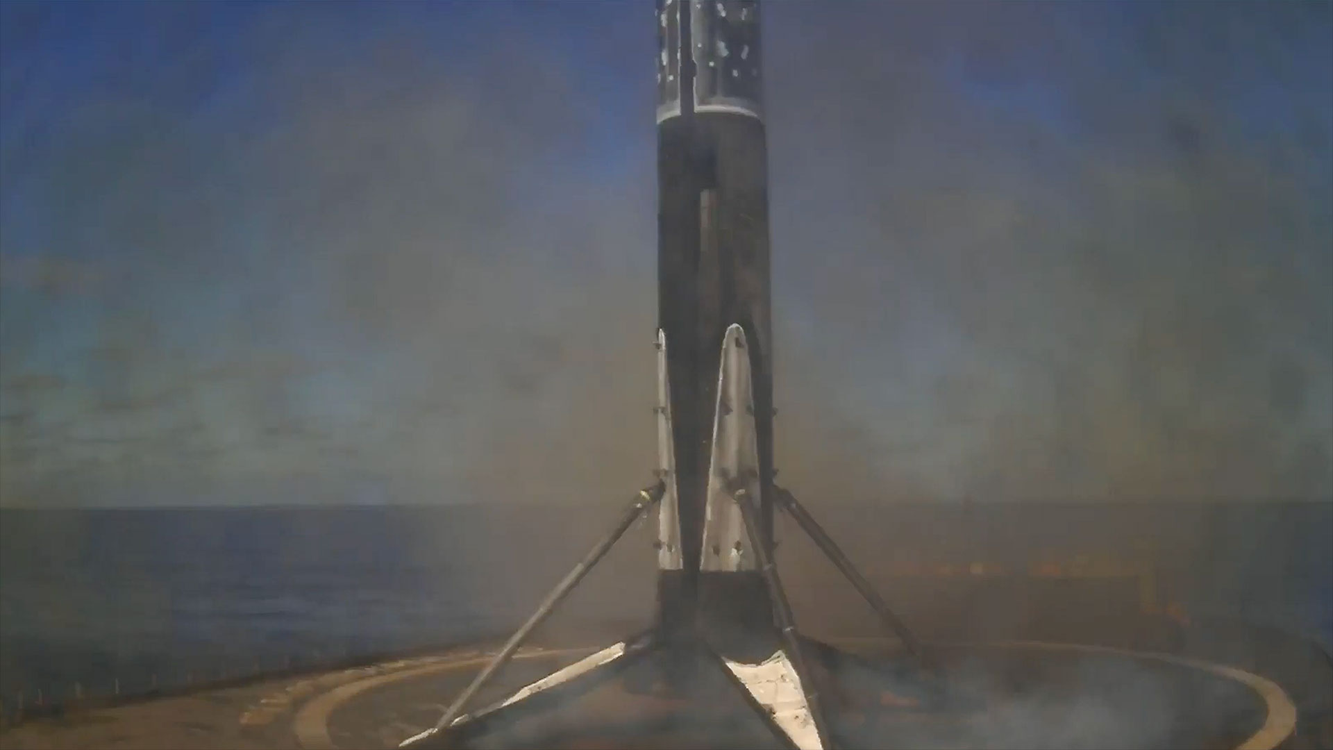 a rocket&#039;s first stage stands on its four deployed landing legs after touching down on a droneship positioned in the ocean