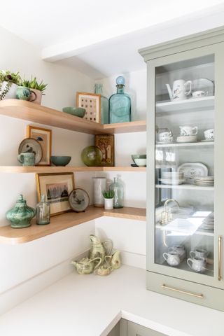 A kitchen with light wooden open shelving and sage green cabinetry