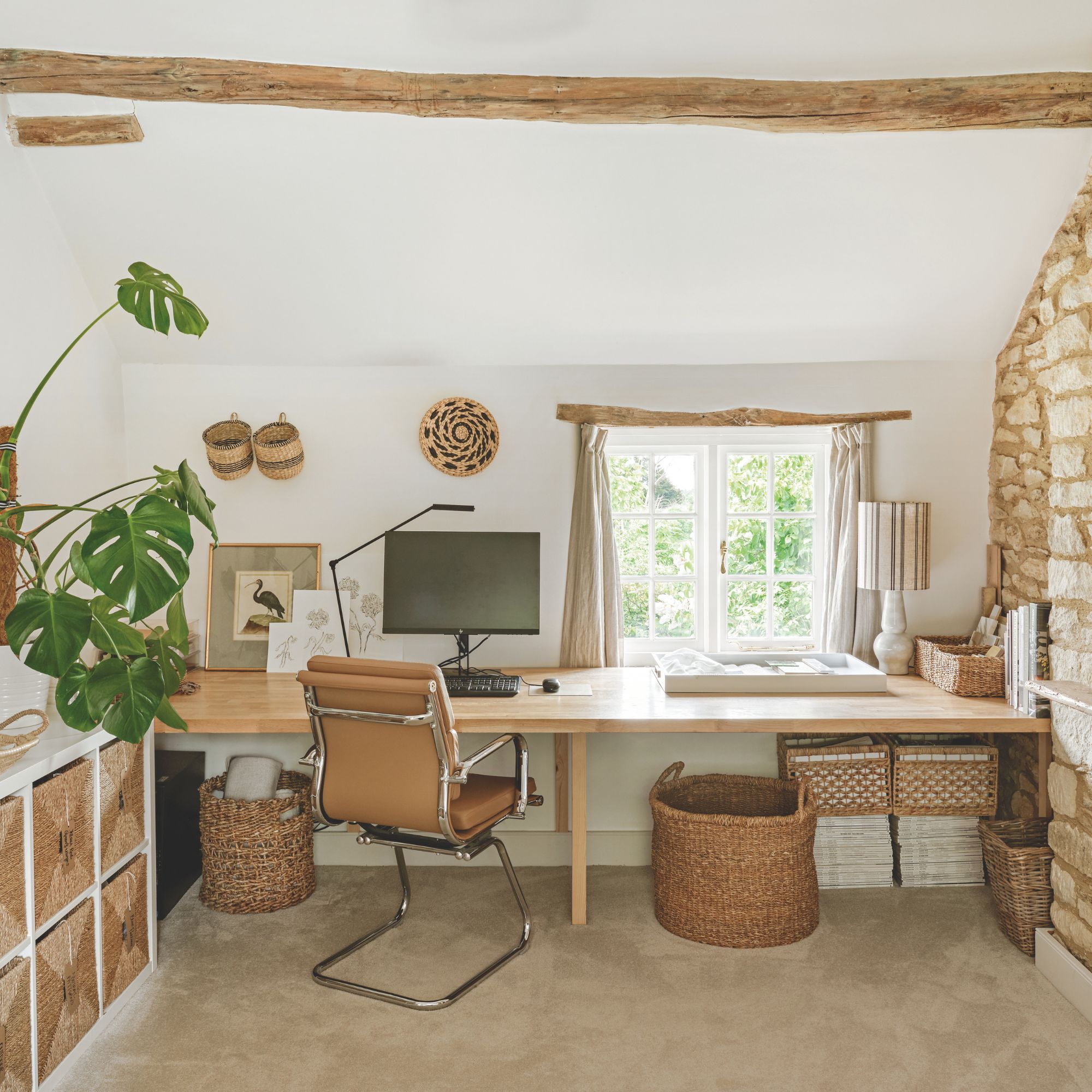 Study in cottage with wooden beam across ceiling, small window, stone wall and large wooden desk with brown leather chair