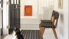 White entryway with black door, black and wooden seats and a striped black and white runner