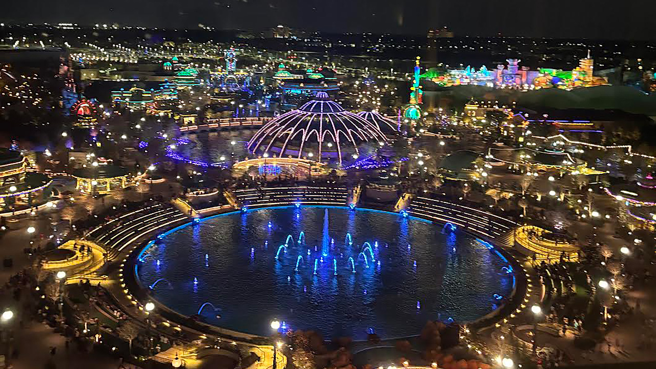 A view of Epic Universe lit up with colorful lights at night from the rooftop of the Grand Helios hotel. 