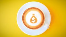 Top view of a coffee cup and latte art showing a money sack with dollar sign