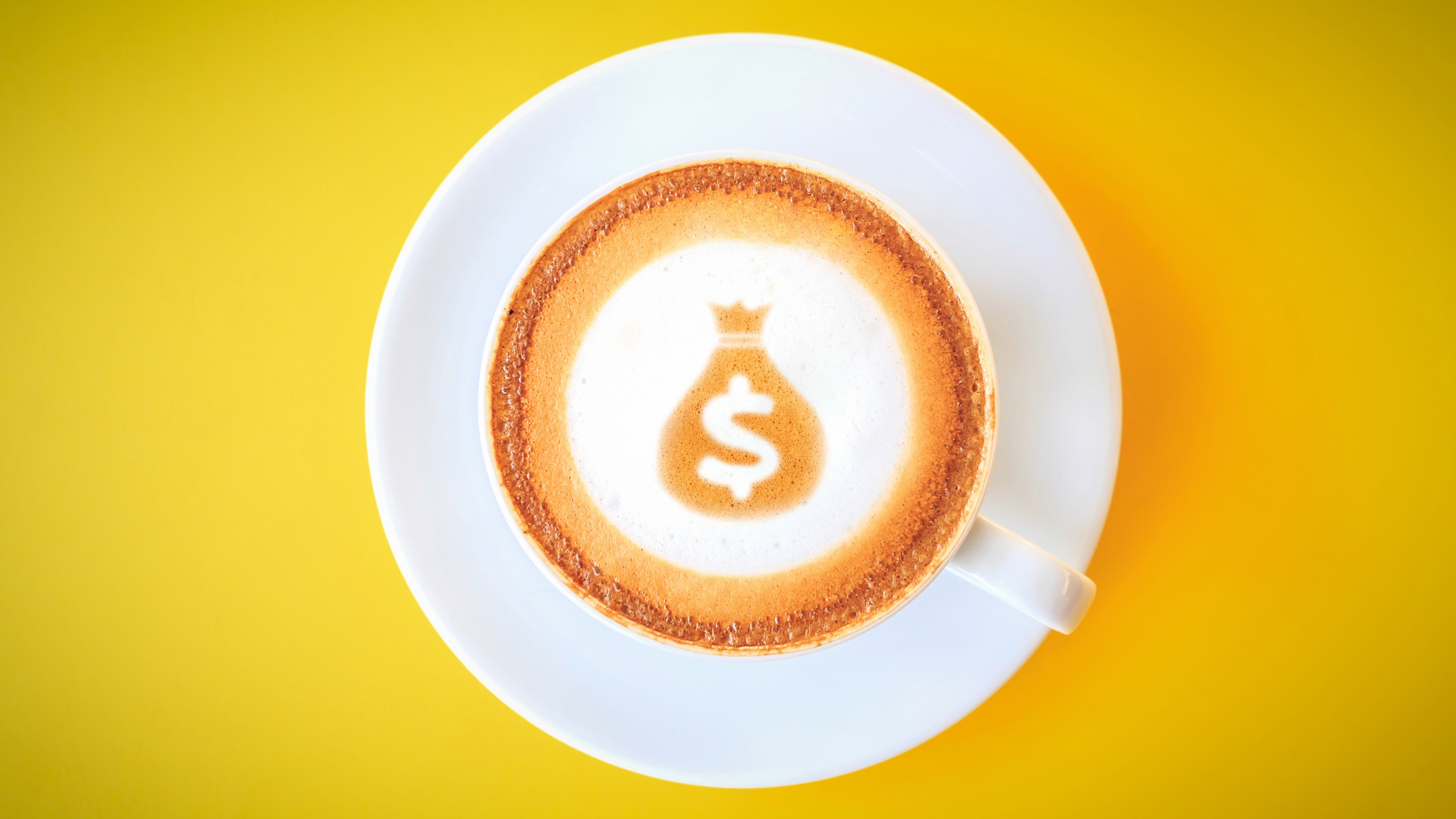 Top view of a coffee cup and latte art showing a money sack with dollar sign