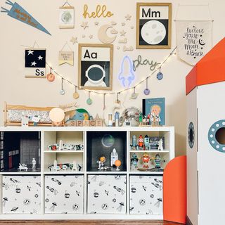 A children's room with a cardboard spaceship and an IKEA KALLAX storage unit with shelf and decorative inserts