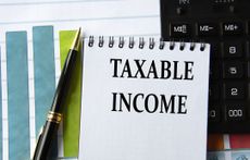 Words that say "taxable income" in a notebook on the background of a calculator, graph, and a pen