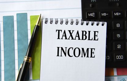 Words that say "taxable income" in a notebook on the background of a calculator, graph, and a pen