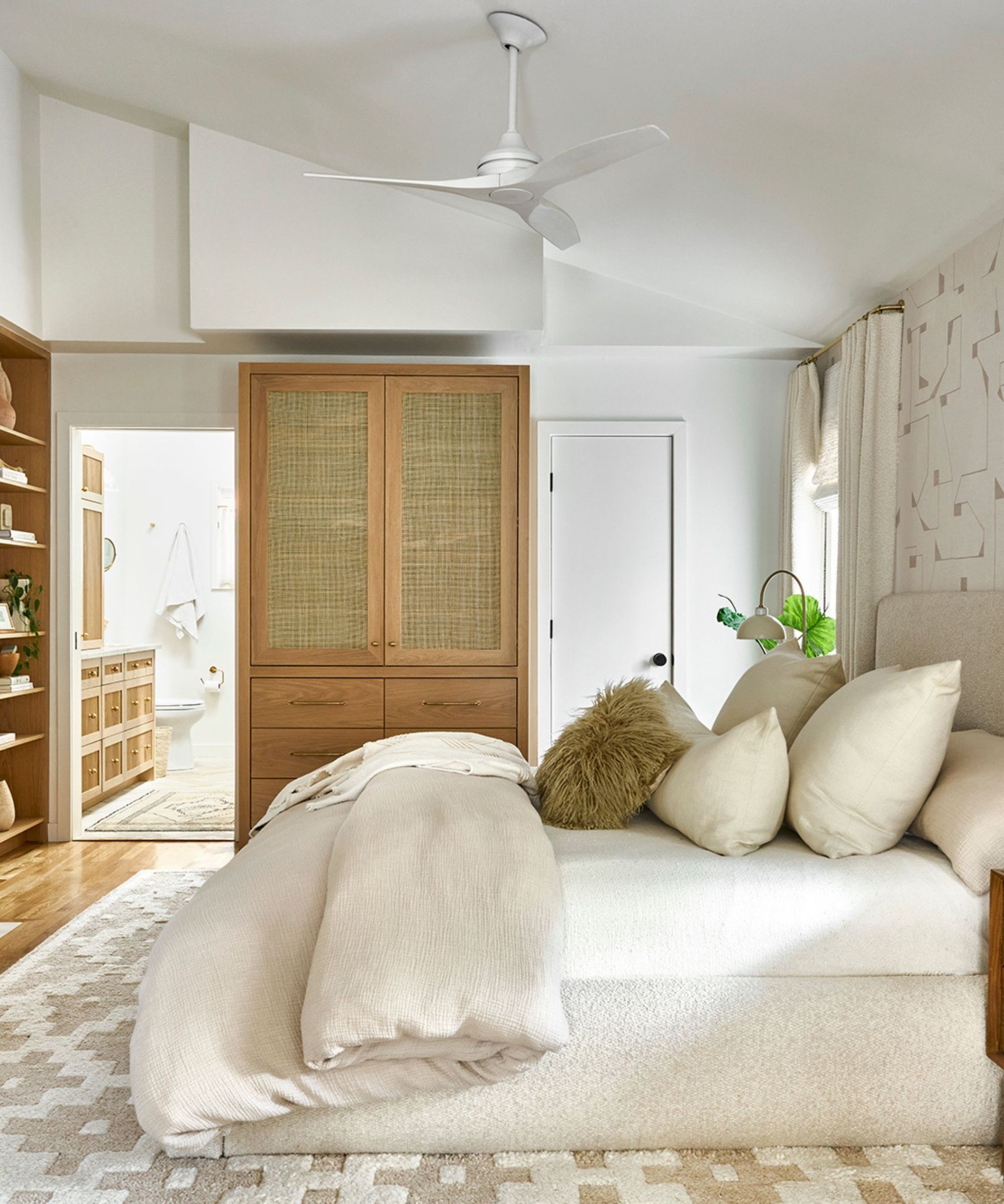 Side view of beige and white cushions on a bed on a white and beige carpet against white walls.