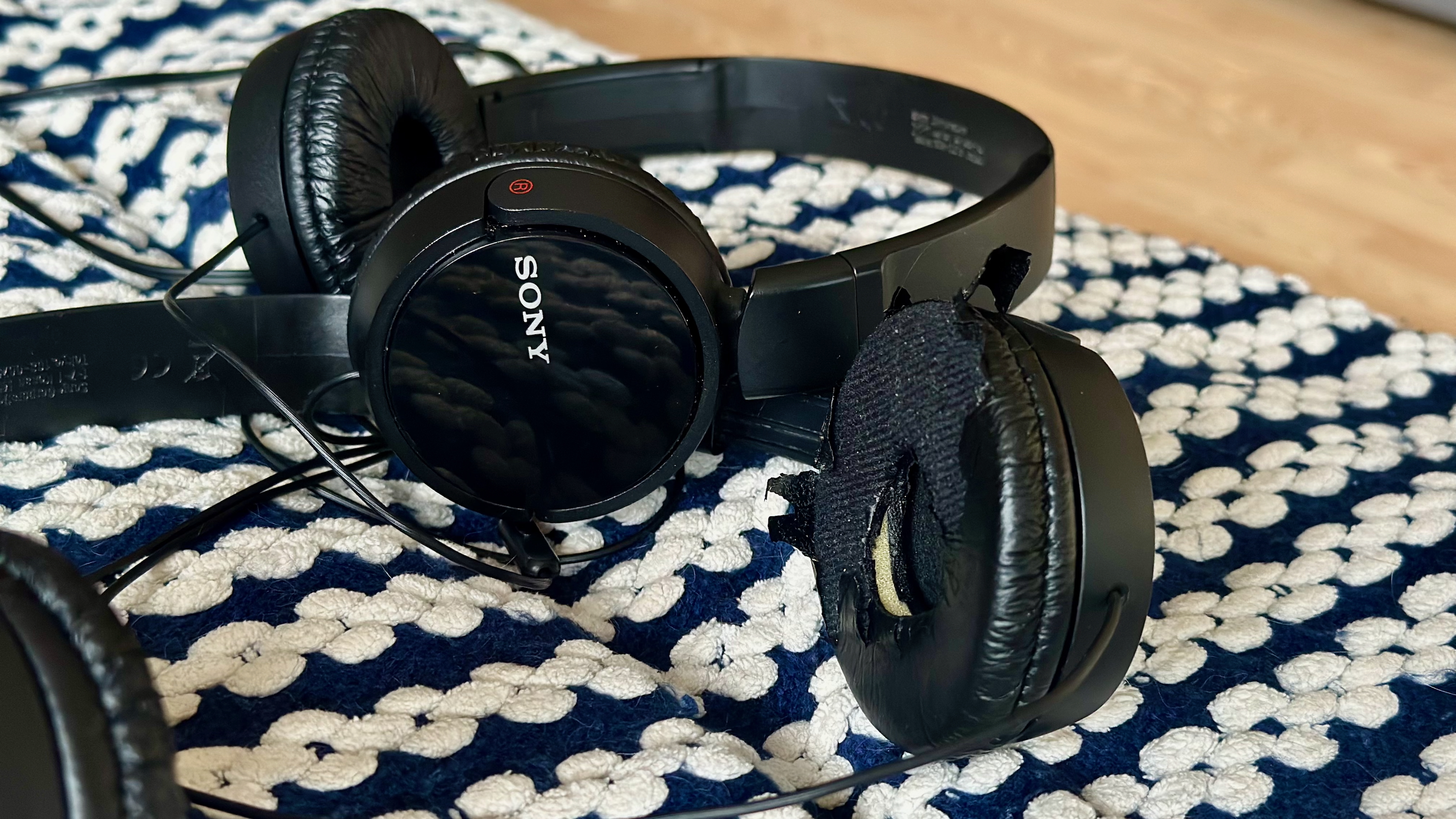 Two pairs of Sony ZX wired on-ear headphones sitting on a blanket, the closer pair notably worn down compared to the other.