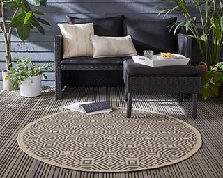 A circular outdoor rug with beige and grey geometric pattern on decking