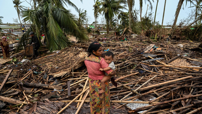 A woman carries her infant child as she looks over destruction wrought by Cyclone Mocha in Myanmar