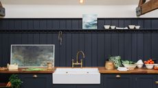 Kitchen with dark blue tongue and groove paneling behind a white sink and along countertops, shelf, wall above painted off white