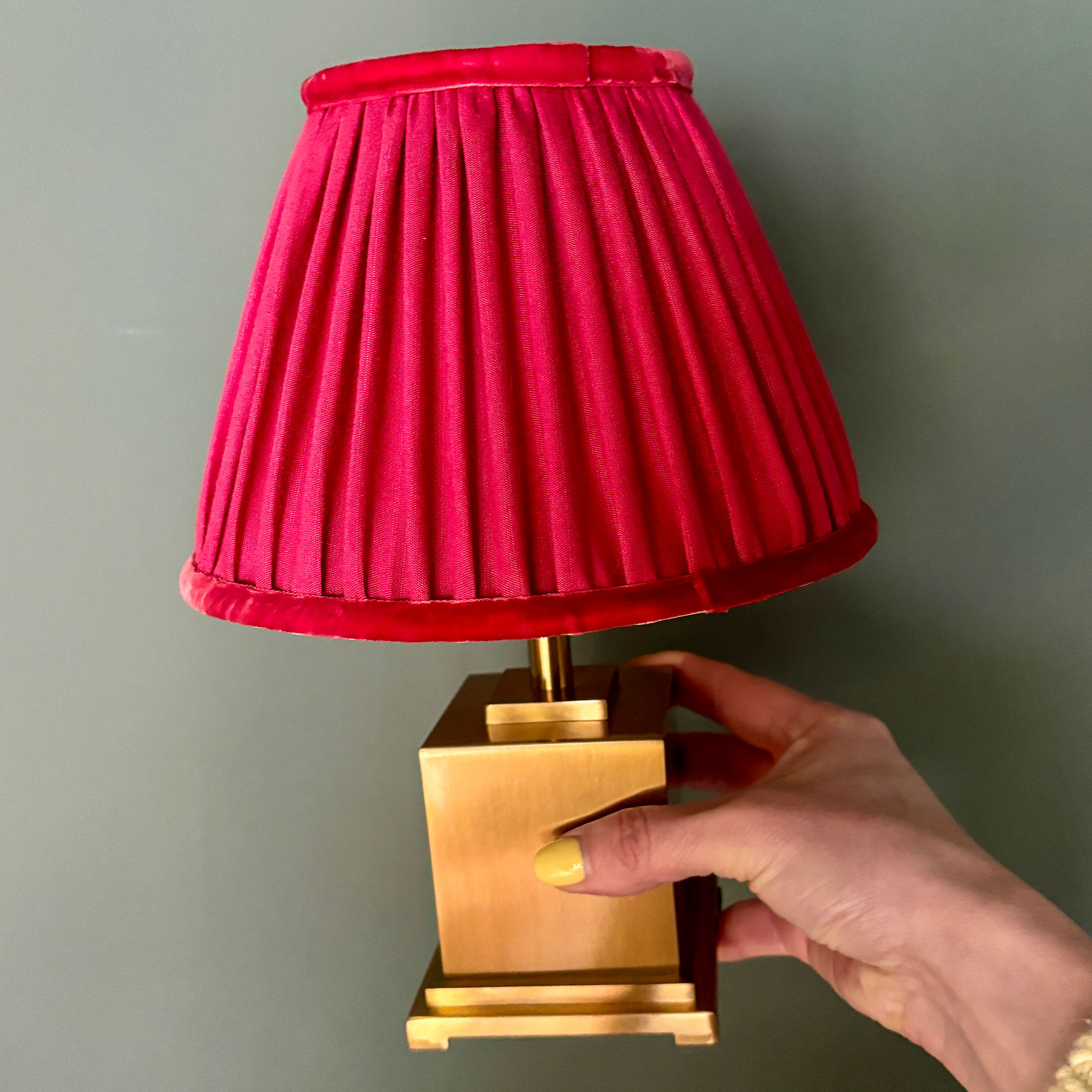 Woman's hand holding square brass lamp with red shade