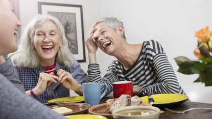 Older women laugh as they sit around a table with desserts.