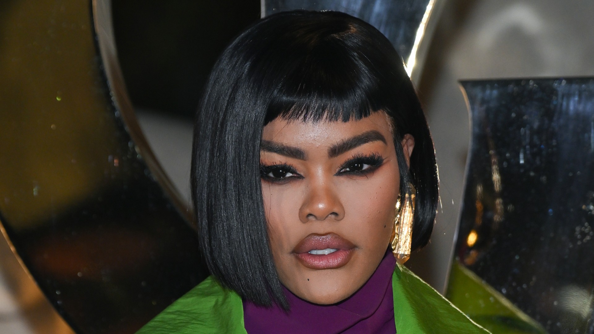 a black woman wears a black bob haircut and dark eye makeup while posing for paparazzi at an event