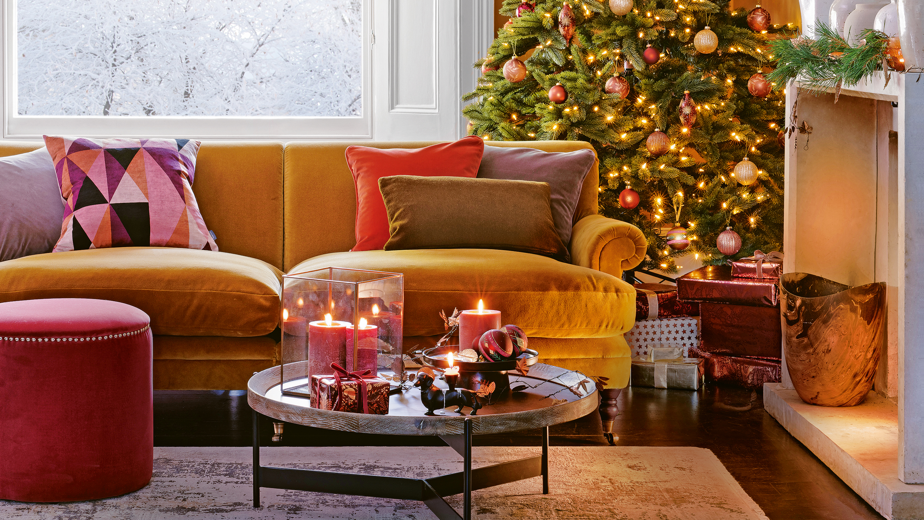 Living room with yellow velvet sofa in front of a beautifully decorated christmas tree, with a fireplace dressed with foliage