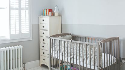White nursery with green painted mountain mural behind a white cot