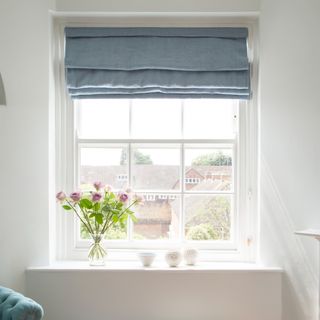 A window with roller blinds and a vase of flowers on the windowsill