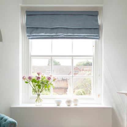 A window with roller blinds and a vase of flowers on the windowsill