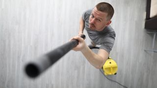 A man using a vacuum cleaner on the ceiling