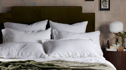 A bed with white linen pillows and a green throw