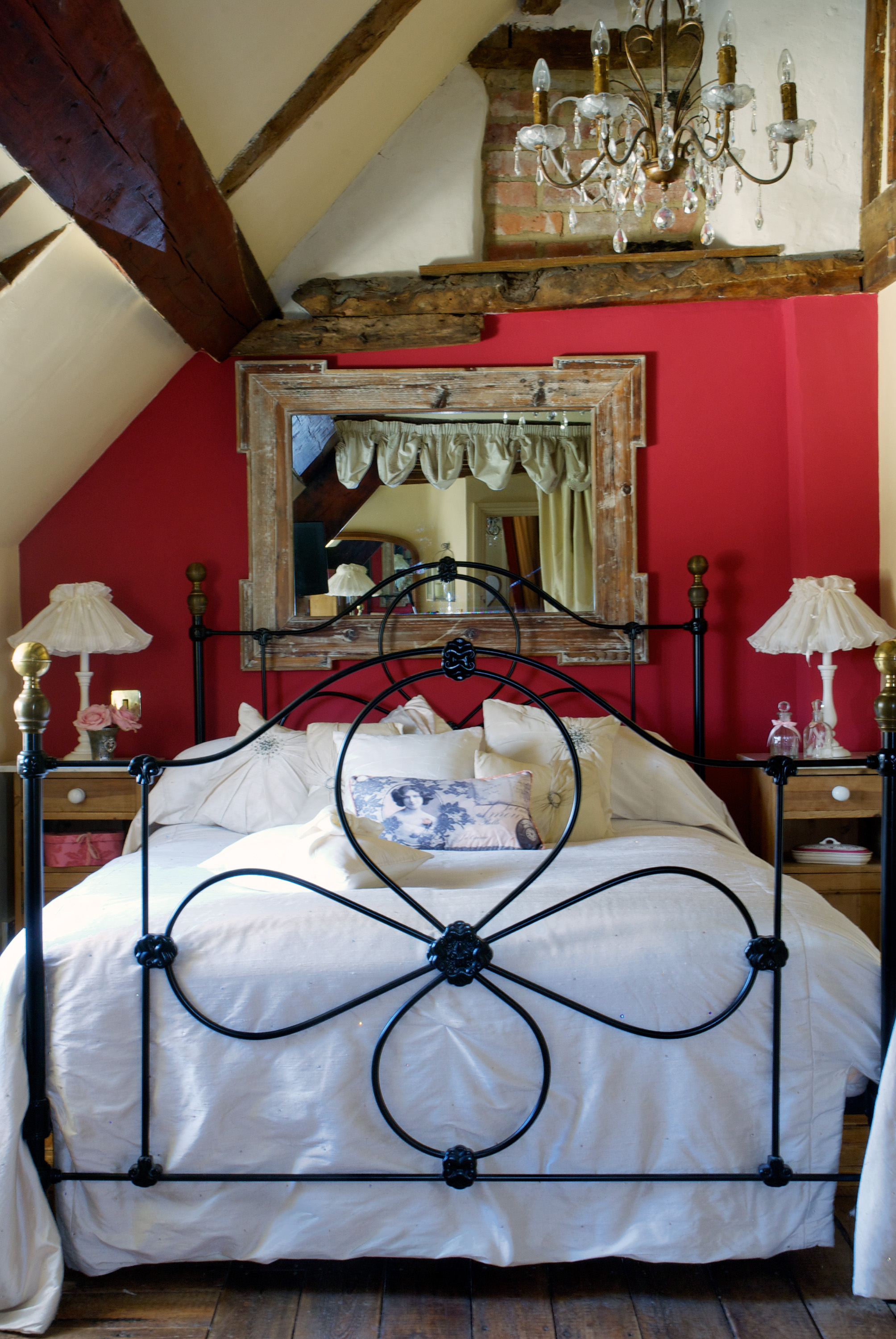 A red bedroom with iron bed mirror, wooden beams and glass chandelier
