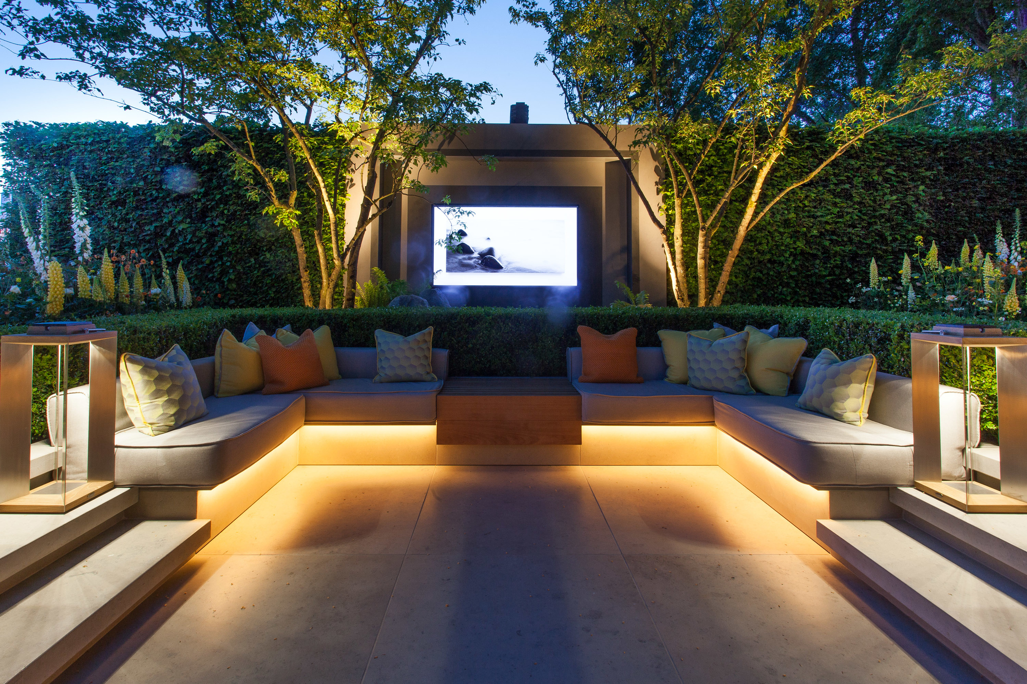 A conversation pit in a modern garden with lighting integrated in the seating area and trees with uplighting in the background