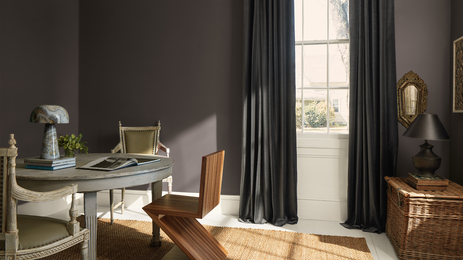 a table and chairs, a basket, a lamp, and wall art in a room with walls painted in Benjamin Moore&#039;s 2026 color of the year, a shade of charcoal gray with subtle notes of espresso titled Silhouette